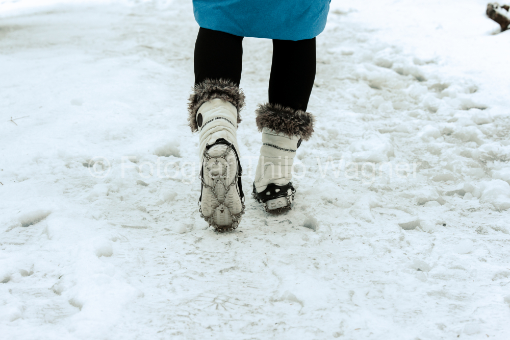 Frau läuft auf einem vereistem Weg mit Grödeln an den Schuhen im Winter